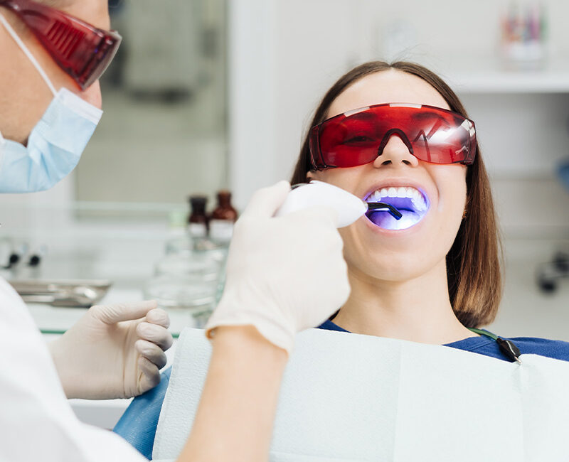 Women with red safety glasses getting her teeth examined by a dentist.